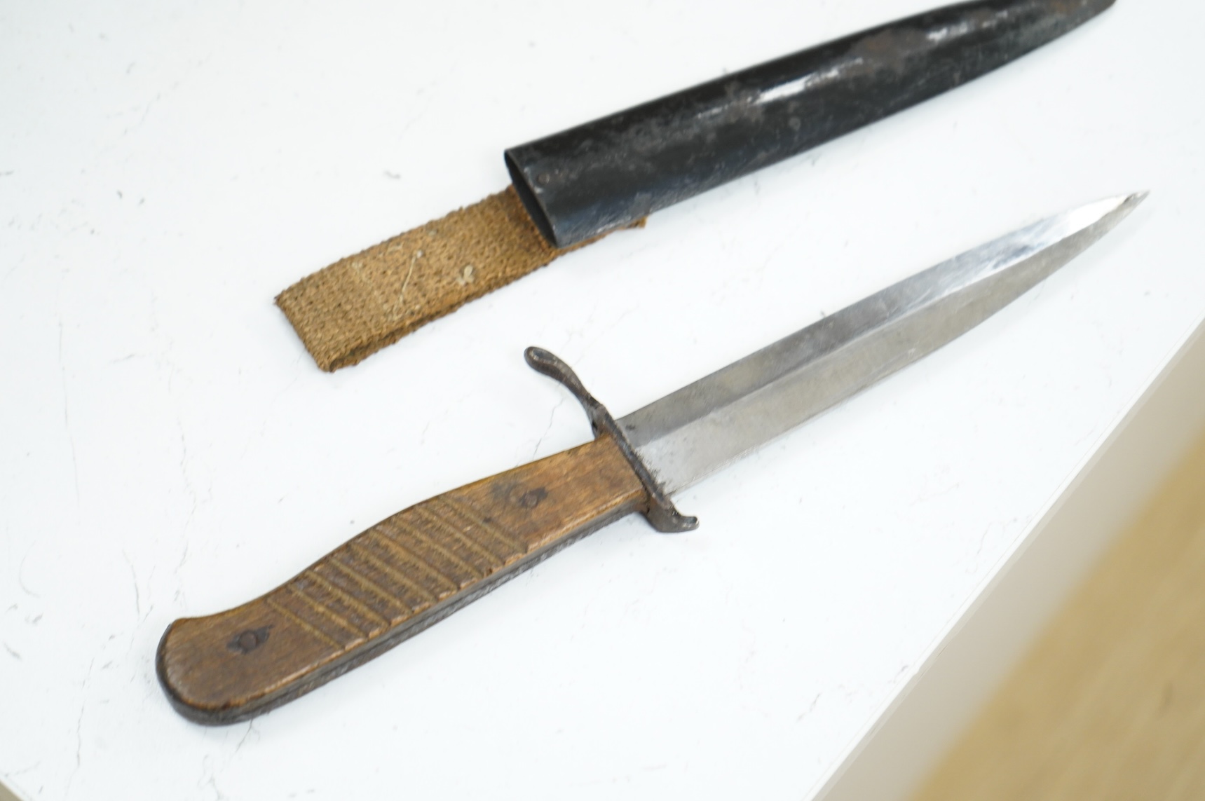 A First World War German Fighting Knife, with two piece wooden grip and steel cross guard, in original steel scabbard with canvas belt loop mount, single edged unmarked blade, blade 14cm, overall 25.5cm.